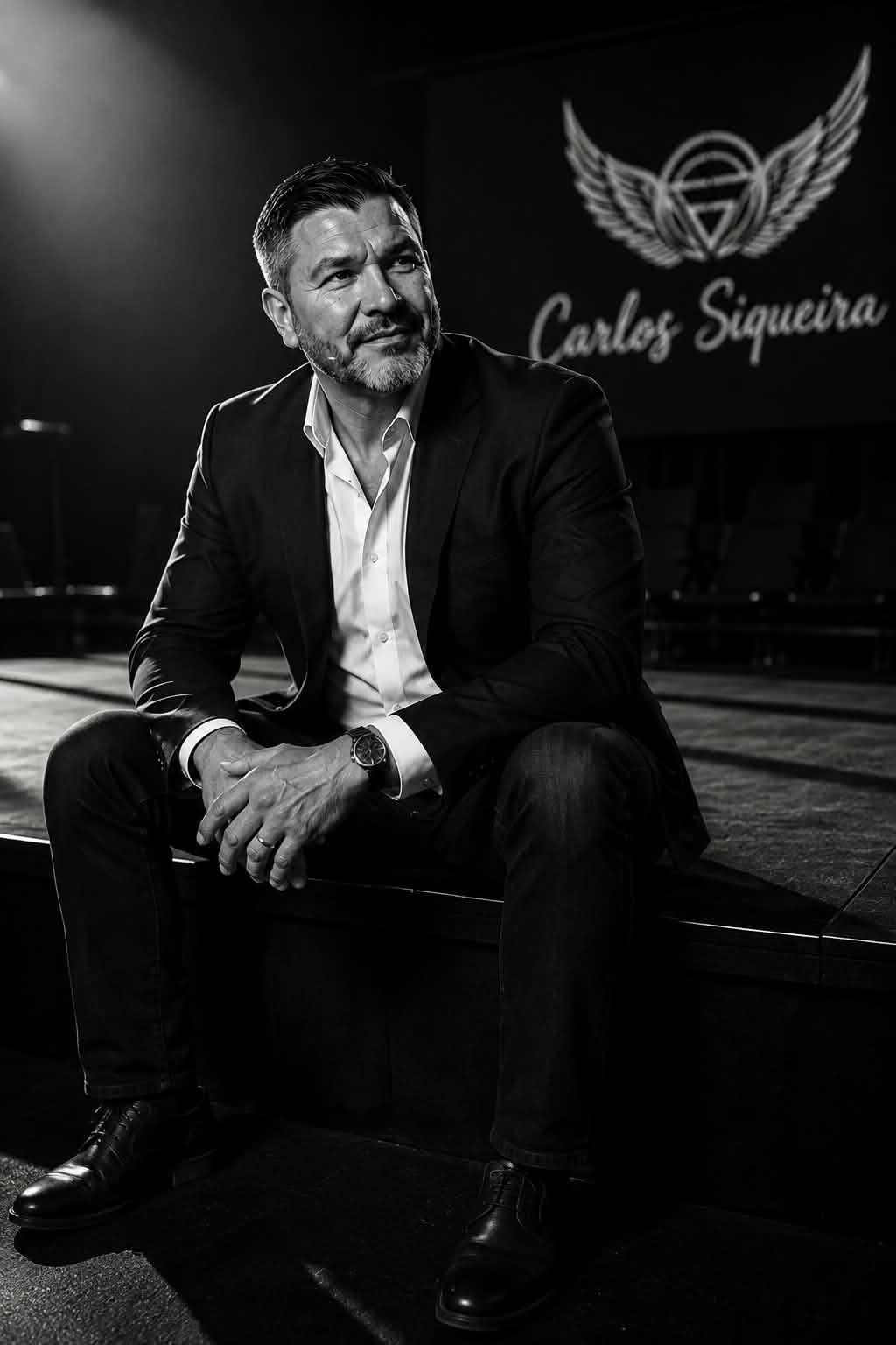 Carlos Siqueira seated on stage in a suit